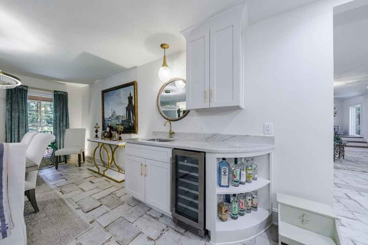 Bar area incorporates white cabinetry, marble countertops, a wine cooler, and a gold-accented mirror.