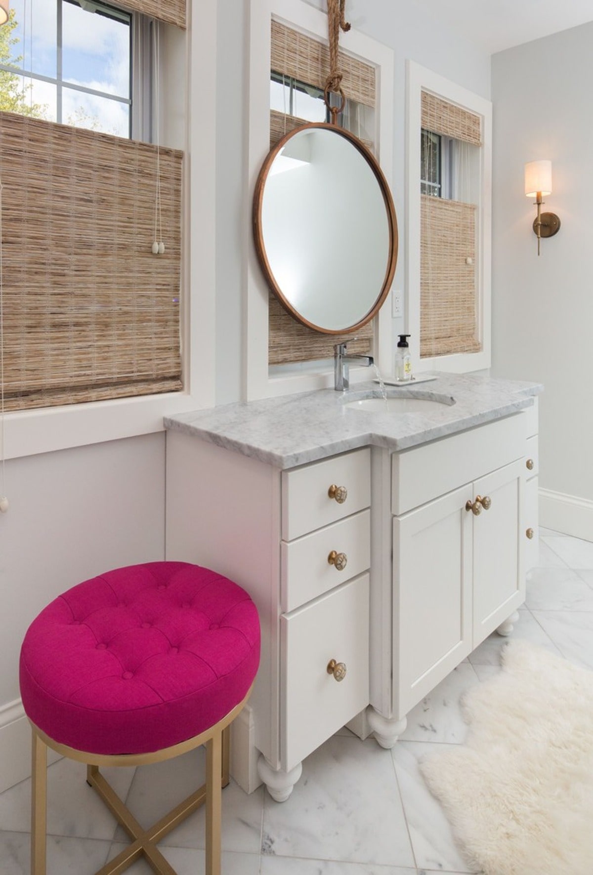 The bathroom's design showcases attention to detail, from the brass hardware on the vanity to the unique pink upholstered stool. The combination of textures and materials creates a sophisticated yet inviting atmosphere.