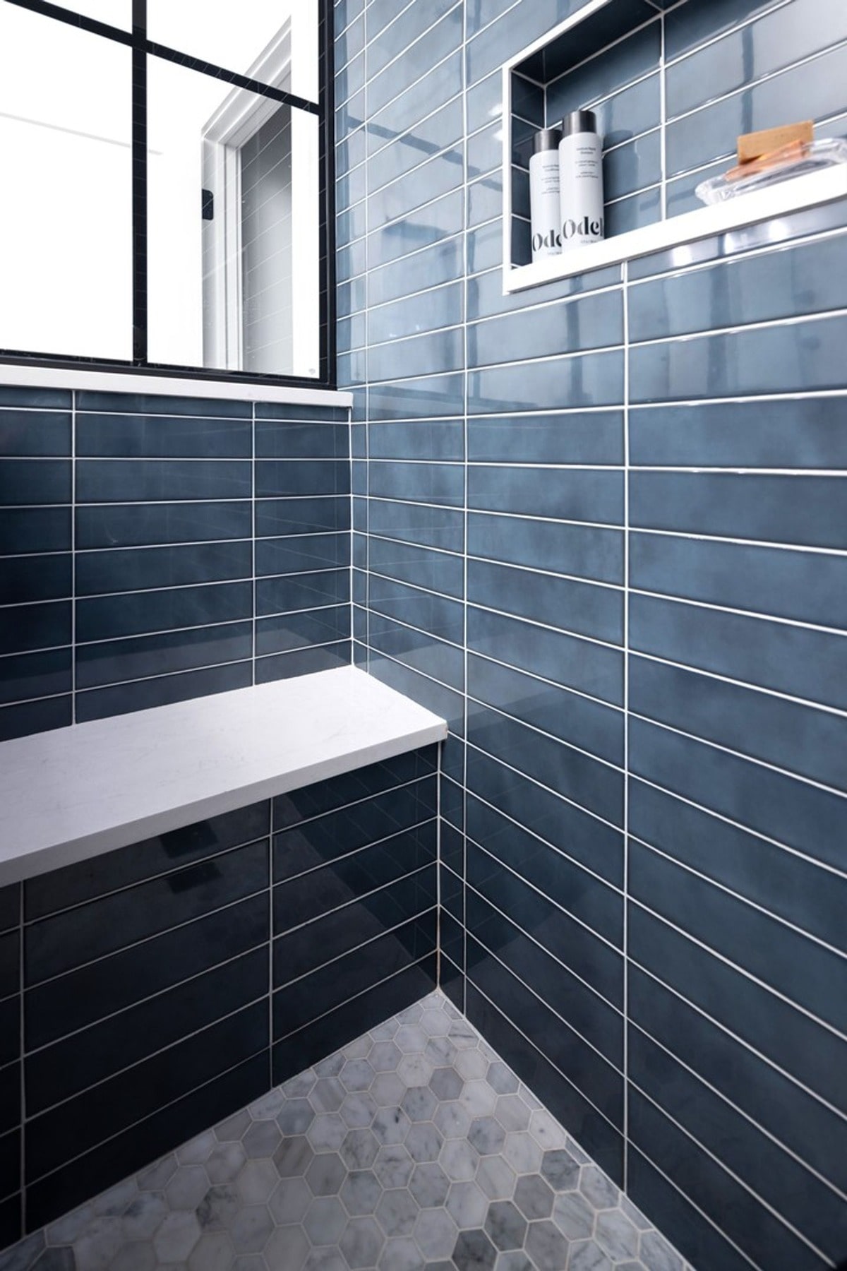 Attention to detail is evident in this stylish shower, from the sleek built-in bench to the recessed niche for toiletries. The combination of dark blue tiles and a lighter-colored floor creates a visually appealing contrast.