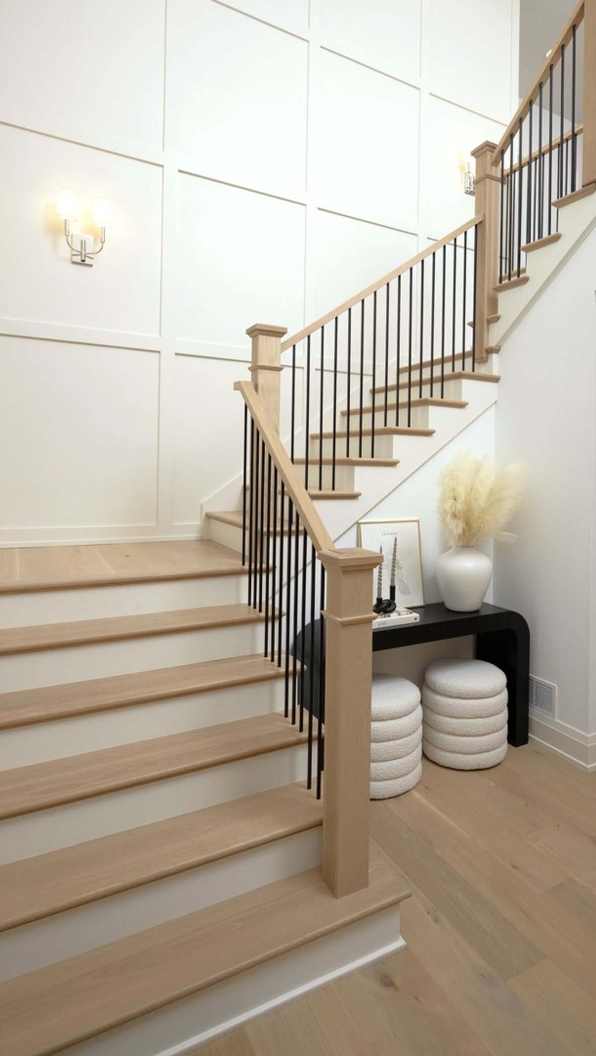 This elegant staircase, with its light wood treads and dark metal railing, creates a striking visual focal point in the home's entryway. The minimalist decor at the landing adds a touch of modern sophistication.