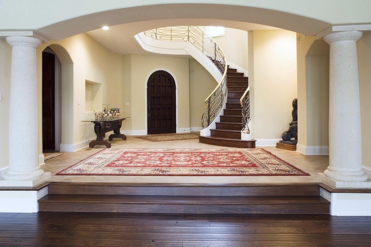 Classical architectural elements, such as the arched entryway and stately columns, are masterfully blended with modern design in this impressive interior space. The curved staircase is a focal point, drawing the eye upward and creating a dramatic sense of scale.