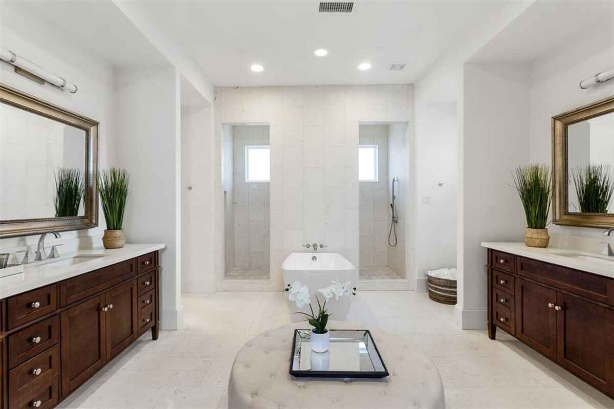 Bathroom features dual vanities with wooden cabinetry, a freestanding tub, and two walk-in showers.