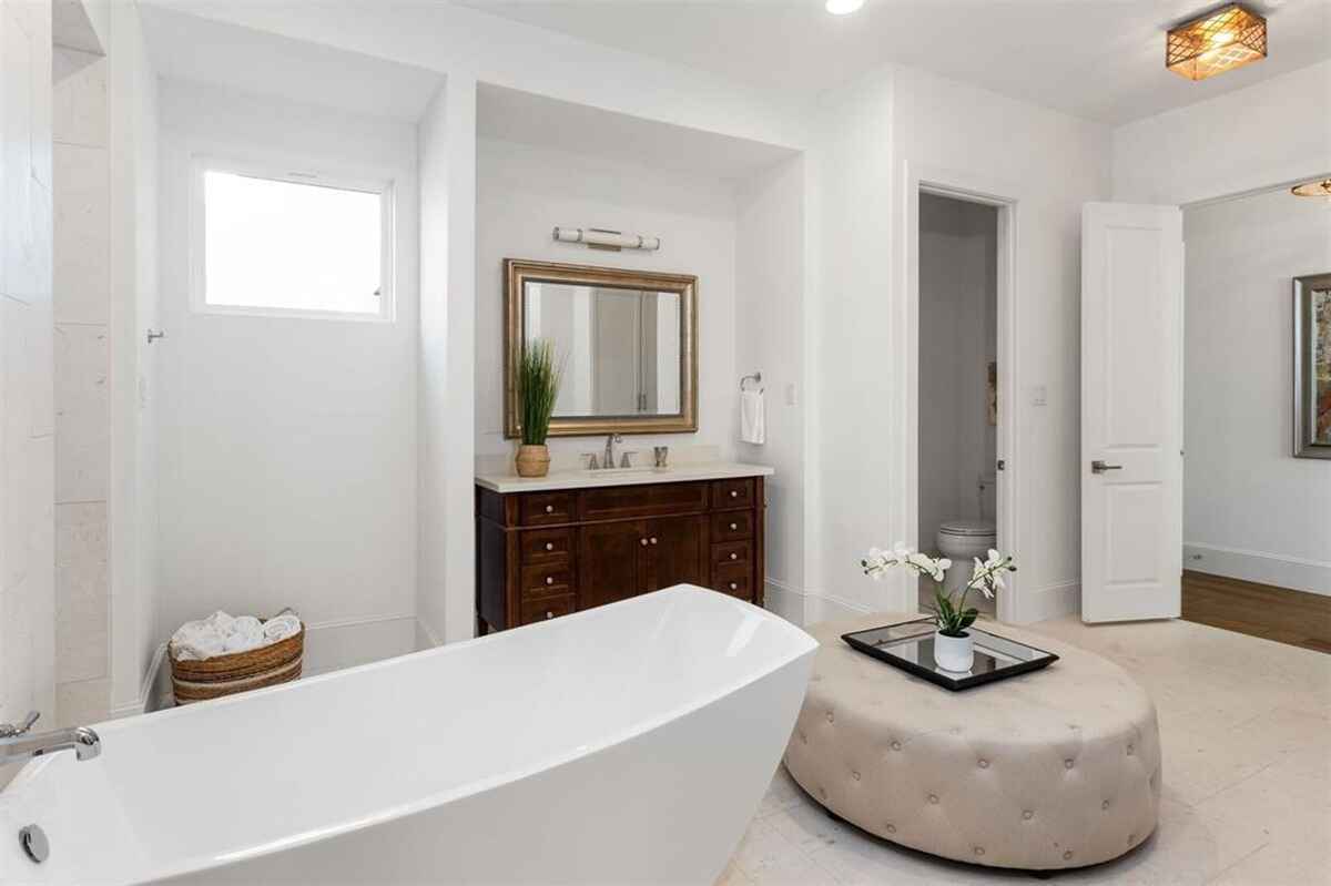 Bathroom includes a freestanding tub, a tufted ottoman, and a private water closet.