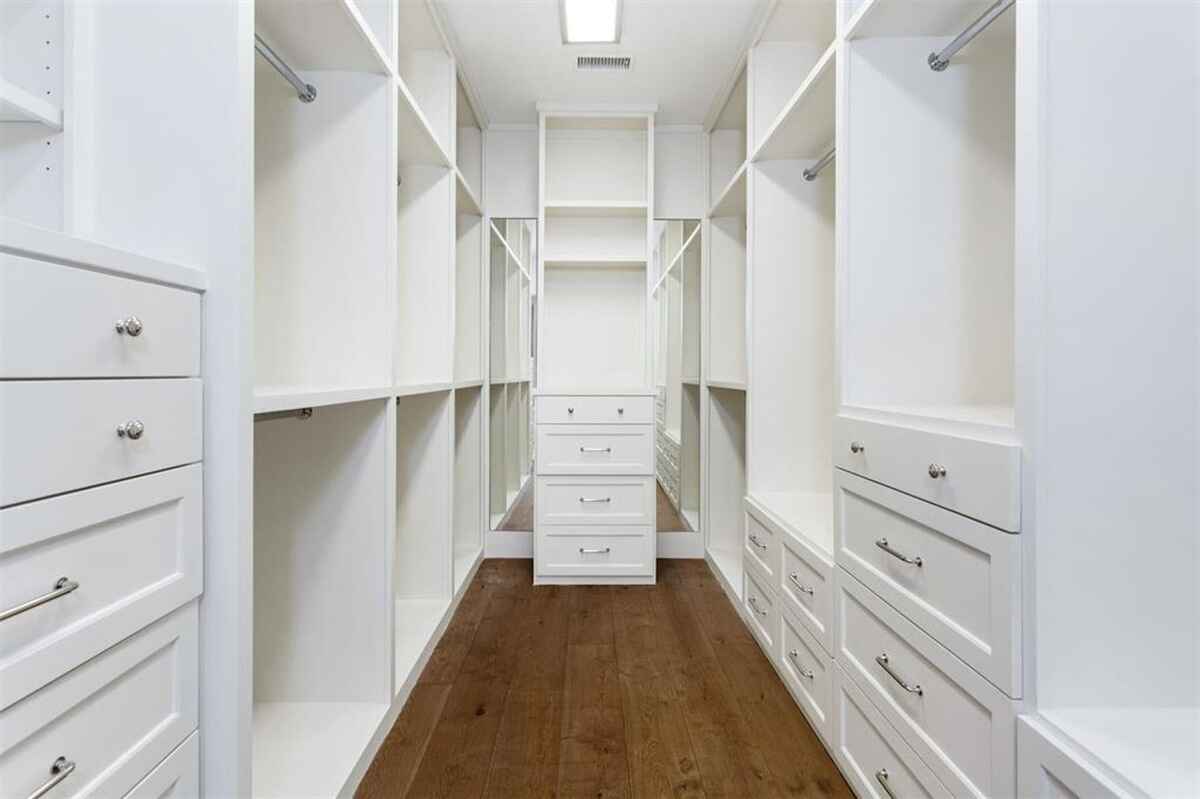 Walk-in closet is equipped with built-in shelving, drawers, and hardwood flooring.