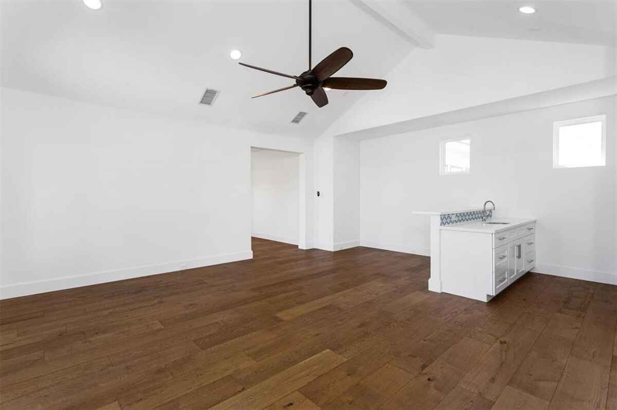 Spacious room features vaulted ceilings, hardwood flooring, and a small kitchenette with white cabinetry.