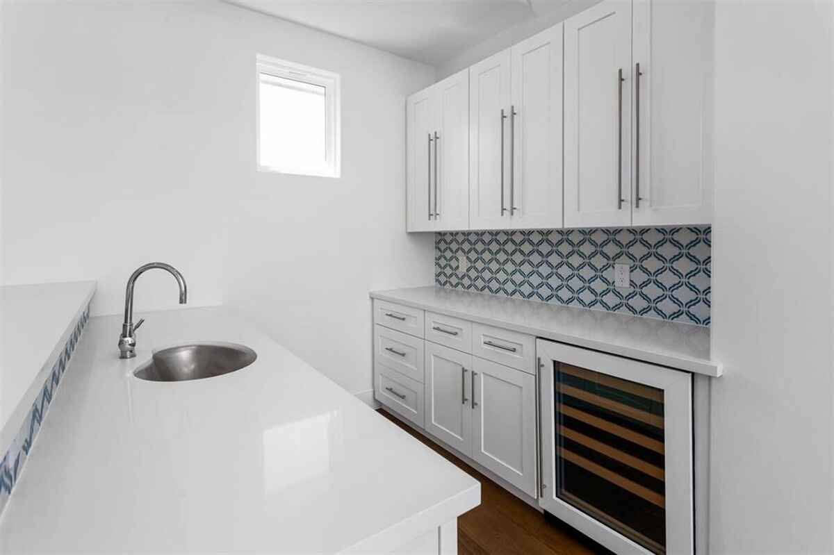  Kitchenette features white cabinetry, a small sink, a patterned backsplash, and a wine cooler.