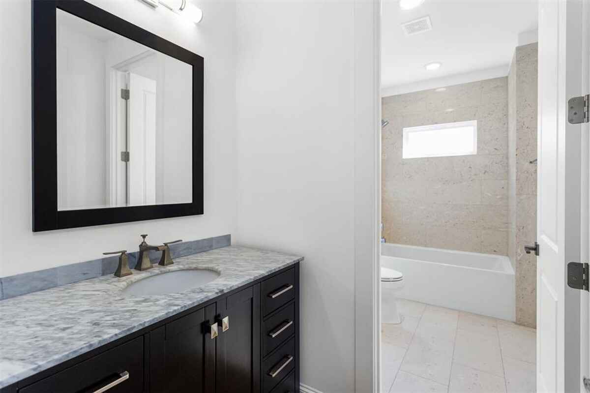 Bathroom includes a marble-topped vanity with a black frame mirror and a connected bathtub with tiled walls.