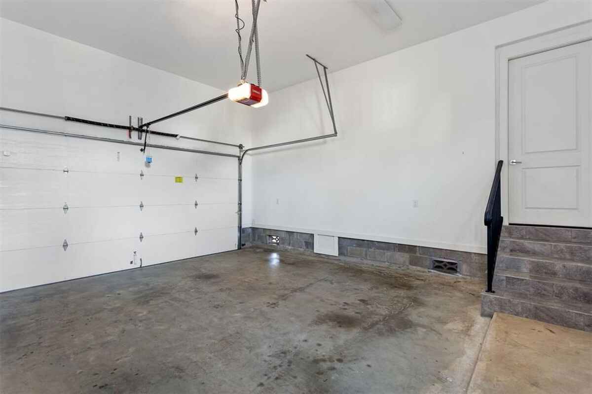 Garage includes a white overhead door, concrete flooring, and a staircase leading to an interior door.