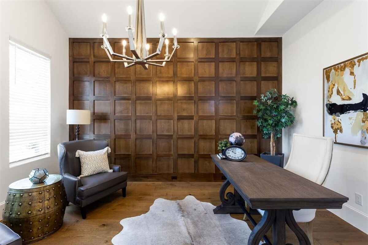 Study includes a wood paneled accent wall, hardwood flooring, and modern furniture arranged around a central desk.