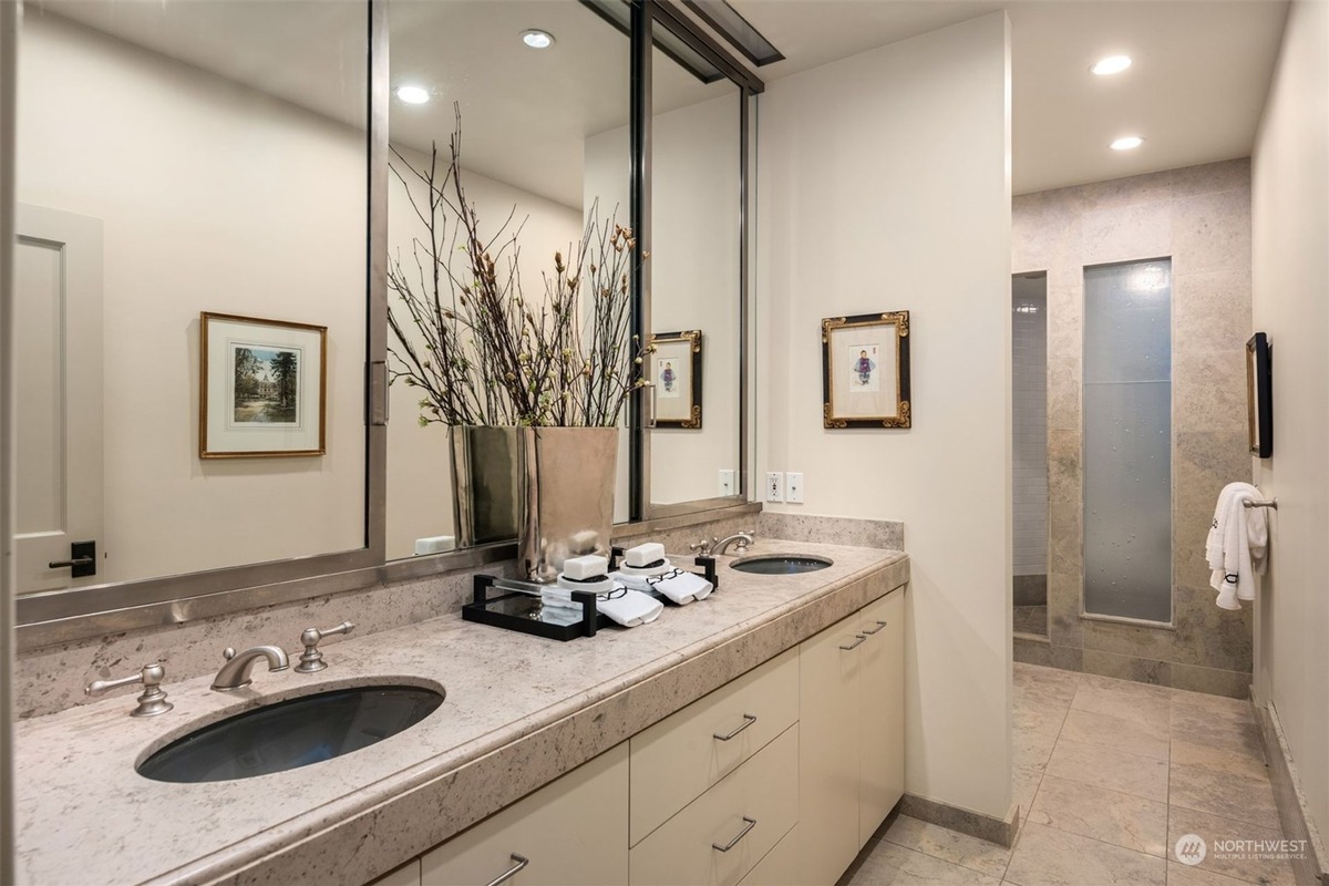 A luxurious bathroom features a double vanity with granite countertops and undermount sinks, framed mirrors, and artwork, all leading to a separate shower.