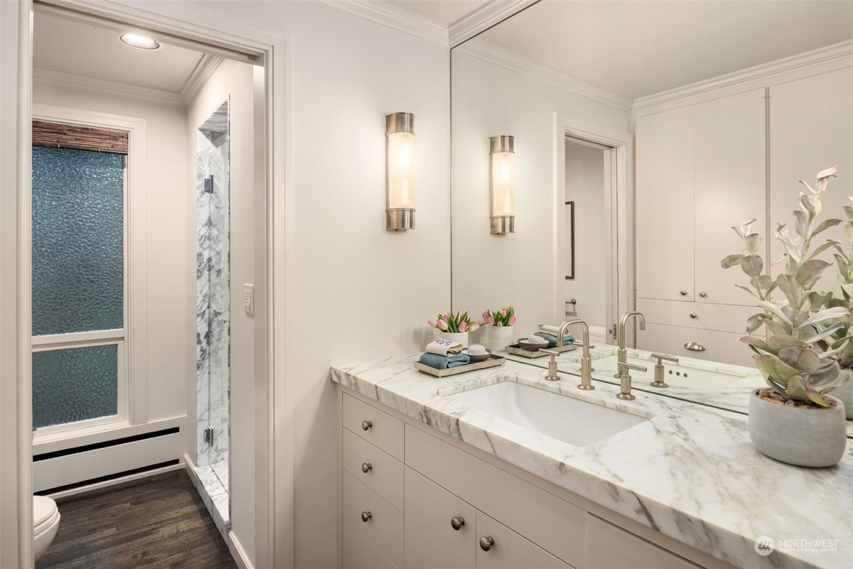 A bathroom with a marble countertop vanity and a large mirror is shown, featuring a separate shower and a plant on the counter.