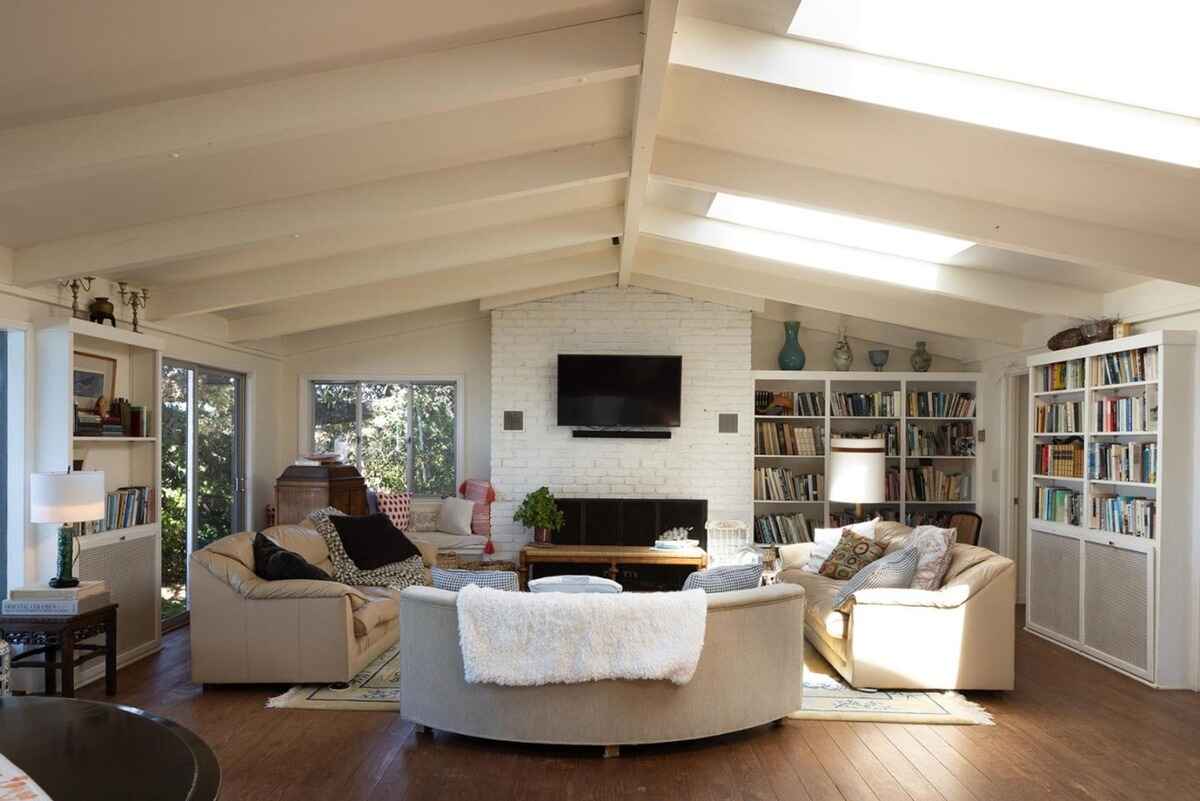 Sunlit living room features a curved sofa, a white brick fireplace, built-in bookshelves, and a vaulted ceiling with skylights.