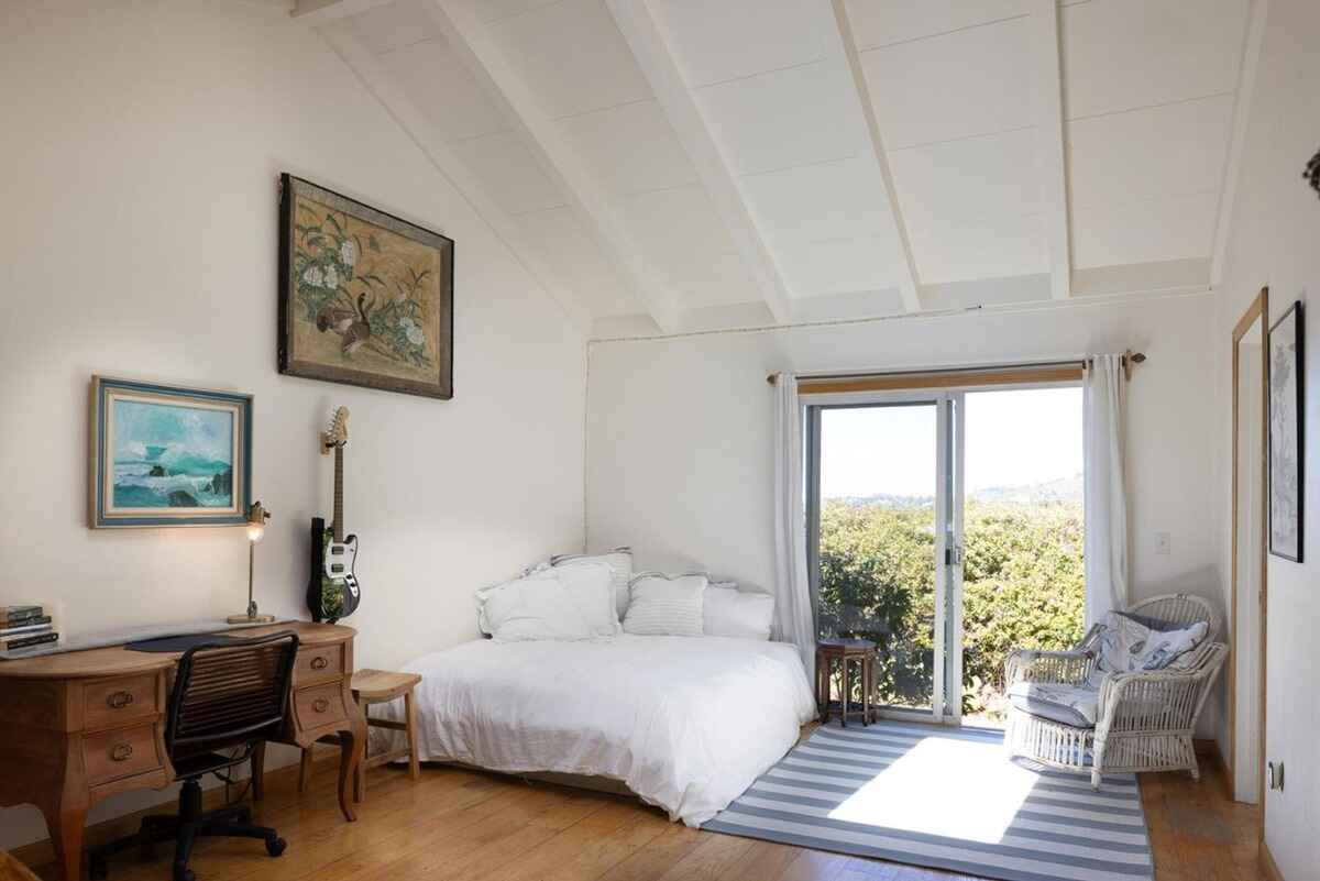 Bright bedroom with vaulted ceilings, a large bed, and sliding glass doors leading to a view of greenery.