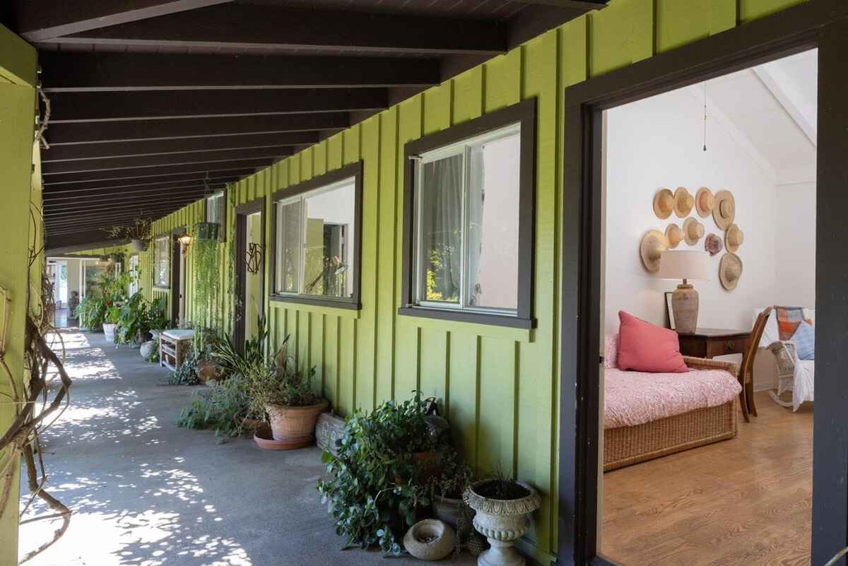 Covered walkway with lime green walls and potted plants offers a view into a room with a daybed and hat decor.