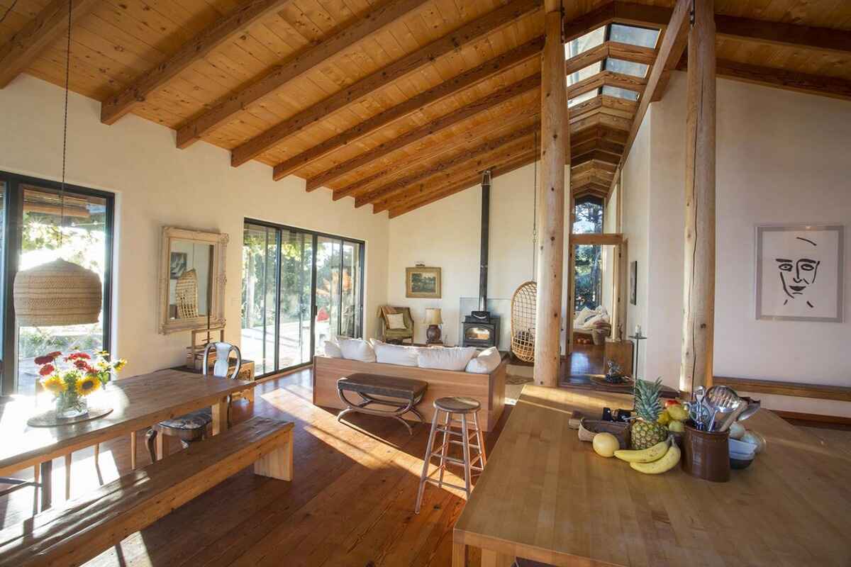 Open-plan living space with wood floors, beamed ceilings, and large windows, featuring a dining table and kitchen area.