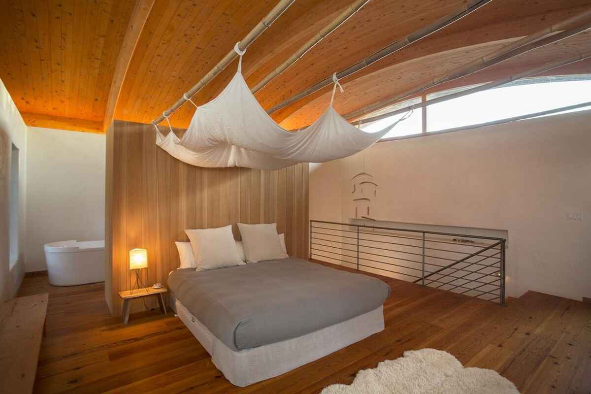 Bedroom with a gray duvet-covered bed, a wood-paneled wall, and a fabric canopy suspended from the ceiling, all under a wood-beamed ceiling.