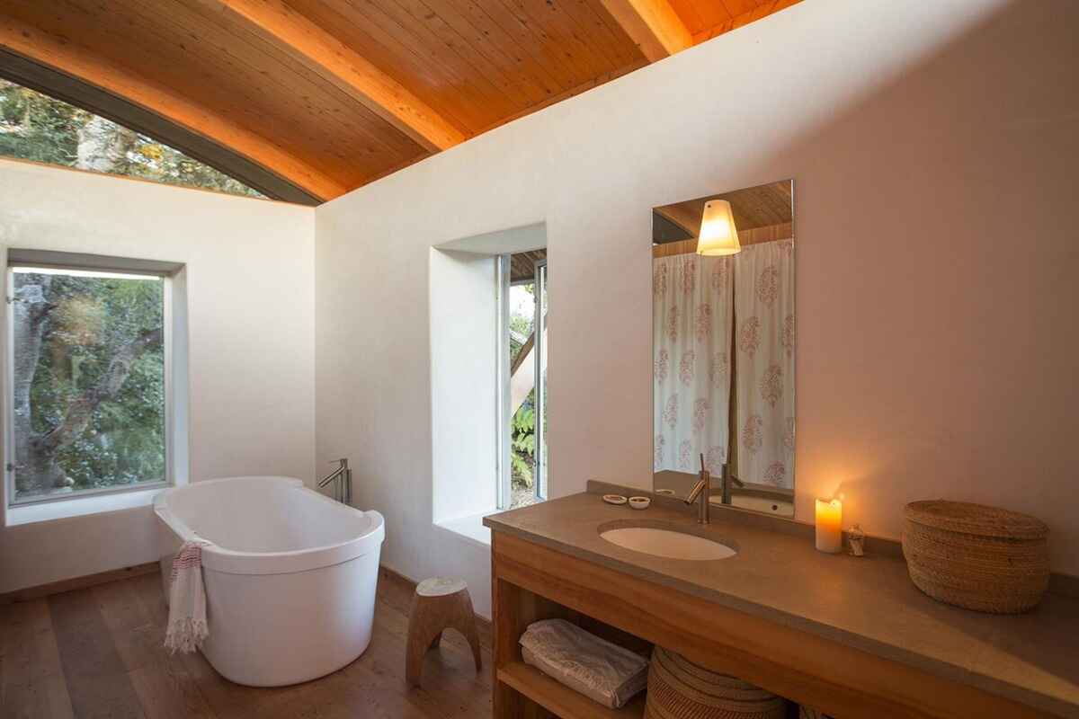 Bathroom with a freestanding tub, wood-paneled ceiling, and a wood vanity with a concrete countertop, all bathed in soft light.