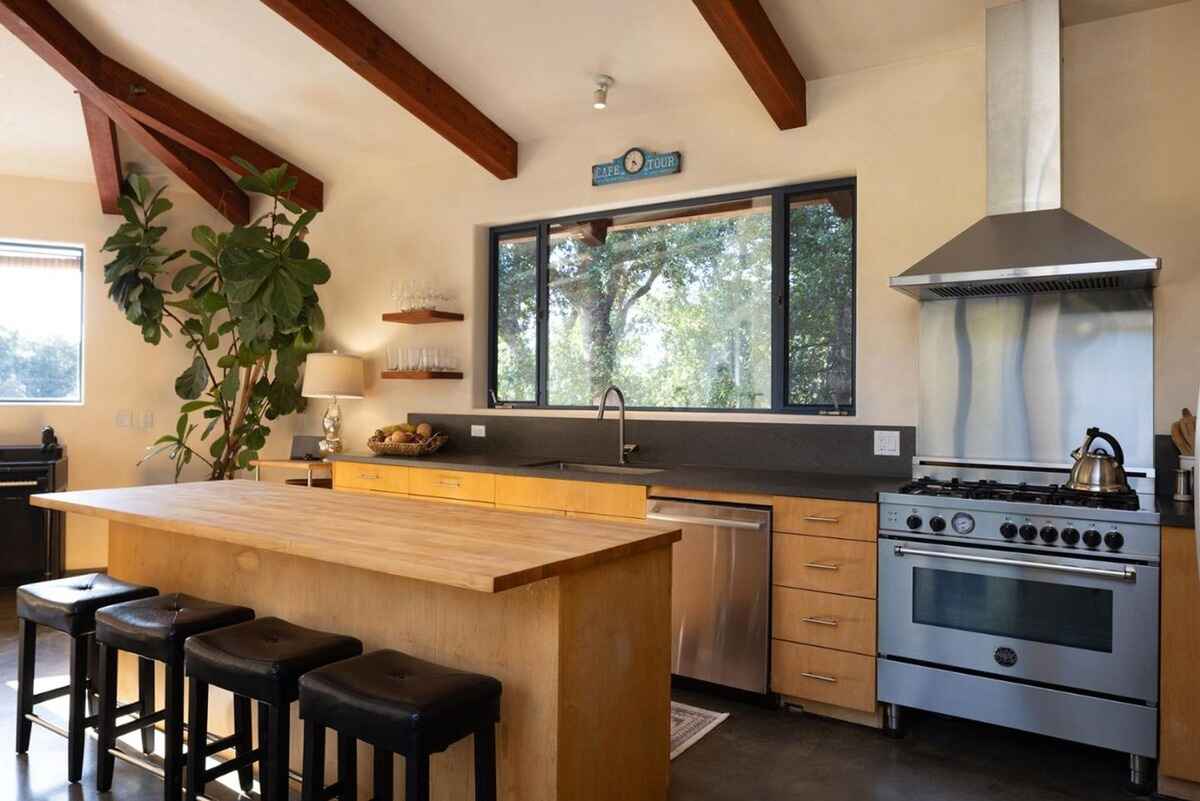 Kitchen with a large wood island, stainless steel appliances, and a wood-beamed ceiling, all enjoying natural light from a large window.