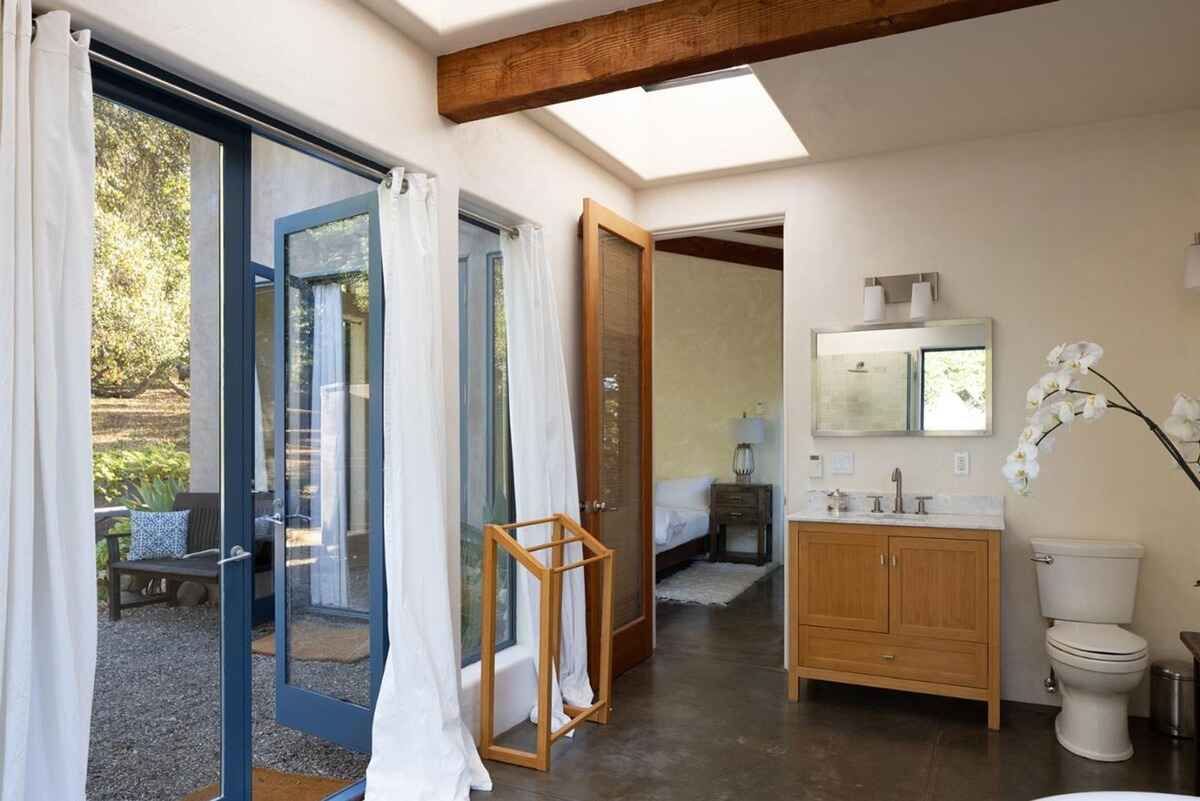 Bathroom with a wood vanity, toilet, and access to an outdoor patio through French doors, all under exposed wood beams.