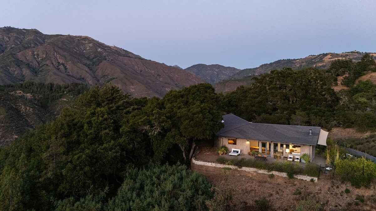 Modern house sits atop a hill overlooking a vast mountain range at dusk.