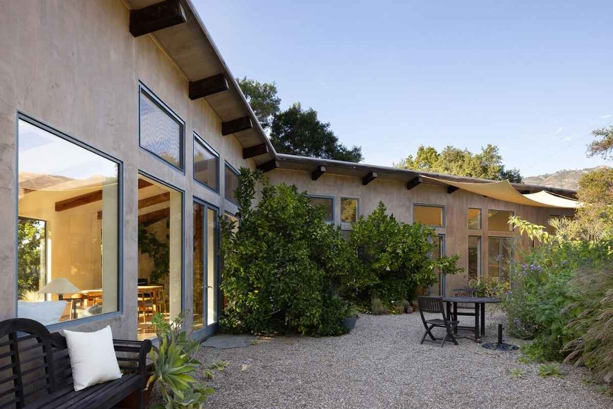 Gravel patio with seating area adjoins a modern home with large windows and a stucco exterior, nestled amongst landscaping.