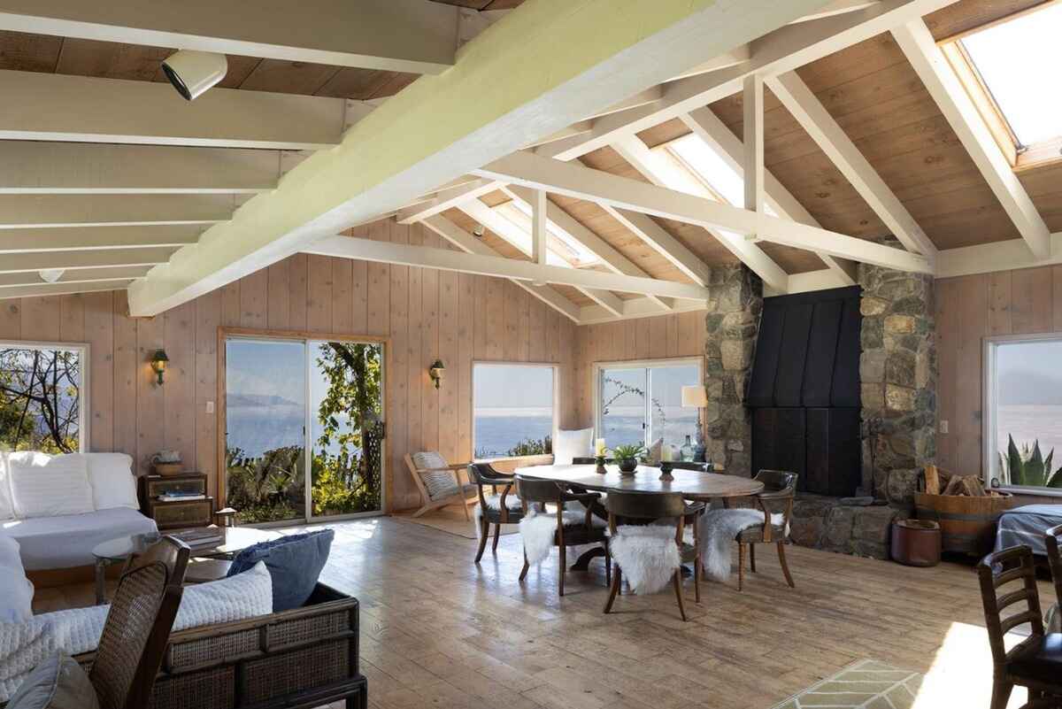 Open-plan living space with vaulted ceilings, wood paneling, and large windows offering stunning ocean views.