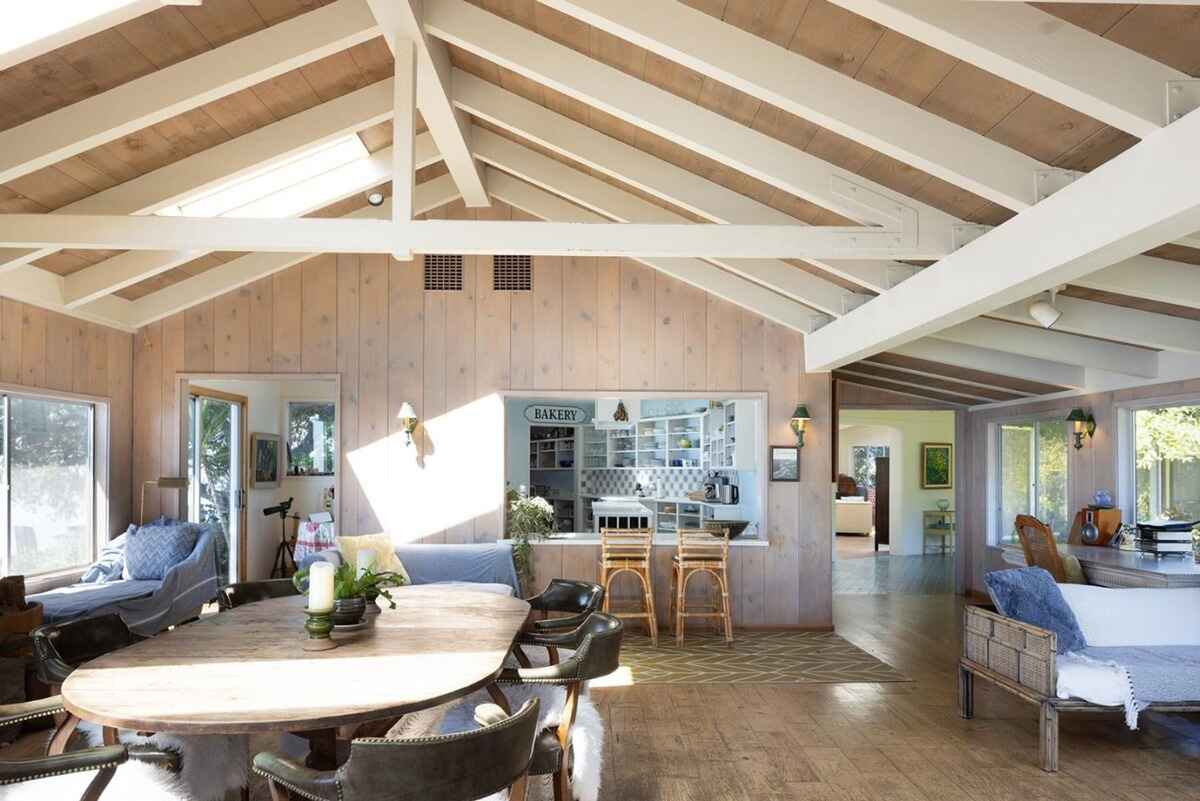 High-ceilinged room with wood paneling, skylights, and a large dining table overlooks a kitchen area.