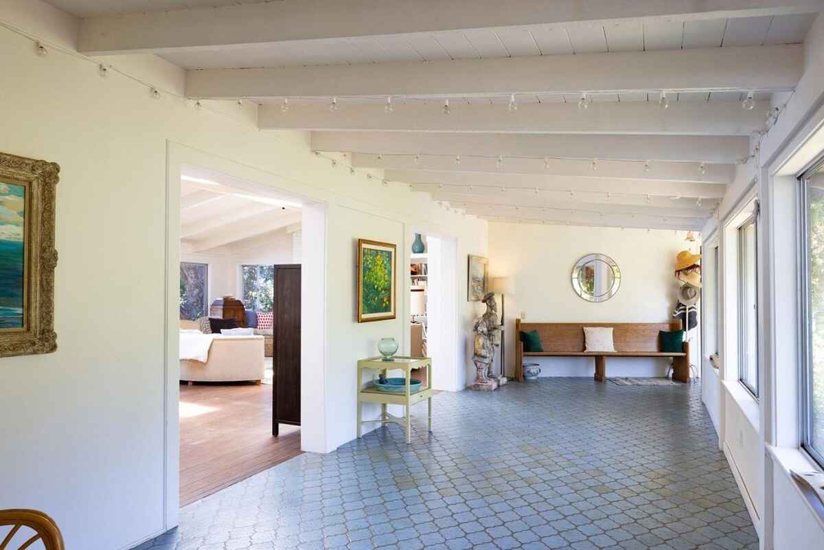 Long hallway with light-colored walls and patterned tile flooring leads to a living area and sunroom.