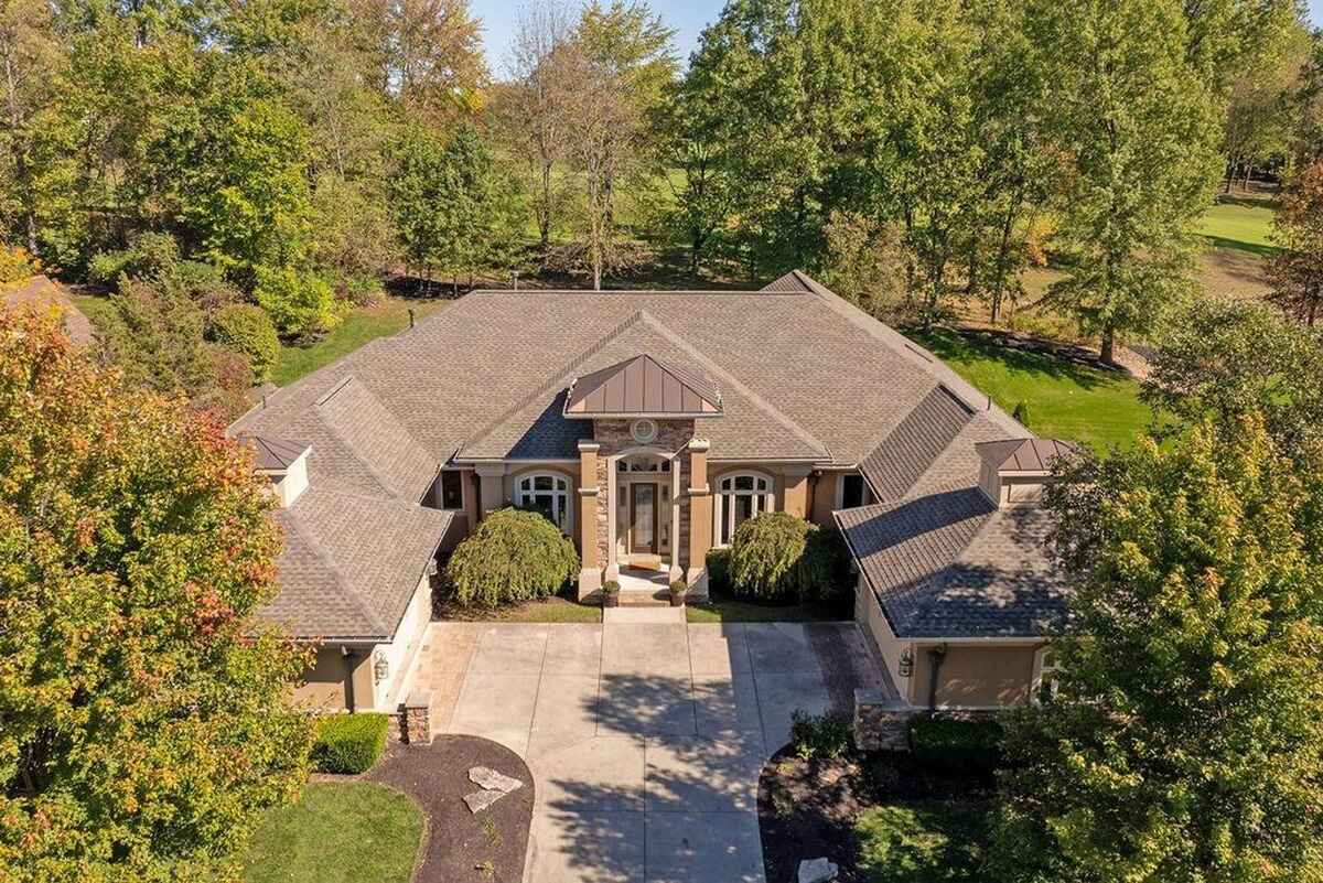 Aerial view showcases the home's front elevation with a lush, tree-lined background and neatly maintained landscaping.