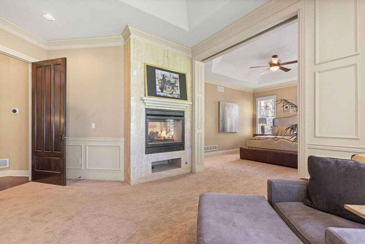 Fireplace and adjoining sitting area with beige walls and wooden accents create a cozy atmosphere.