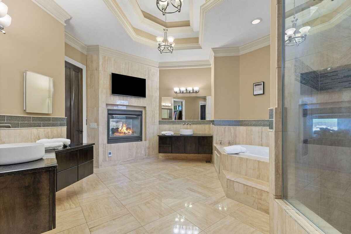 Large bathroom featuring a two-sided fireplace, walk-in shower, soaking tub, and a double vanity with modern fixtures.