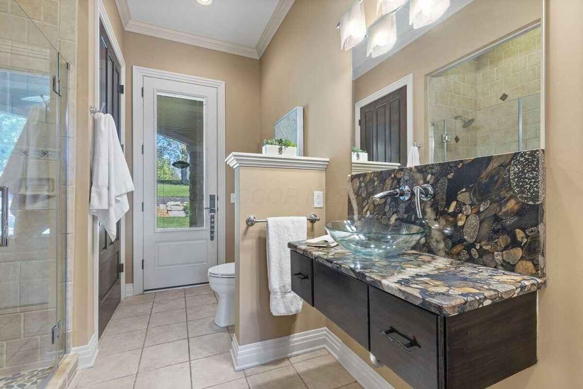 Compact bathroom with a unique stone countertop, glass vessel sink, and direct access to an outdoor area.