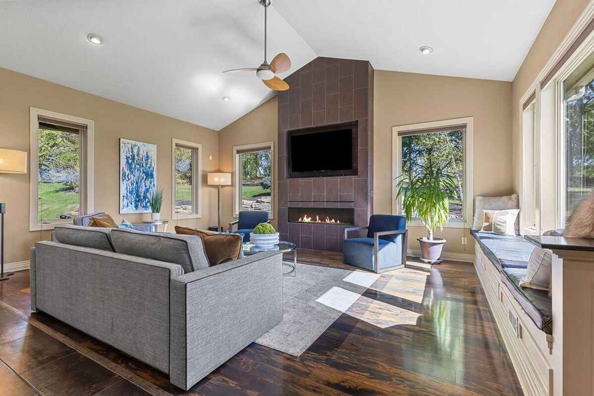 Living room features a tiled fireplace, wall-mounted TV, expansive windows, and a cozy seating area with natural light.