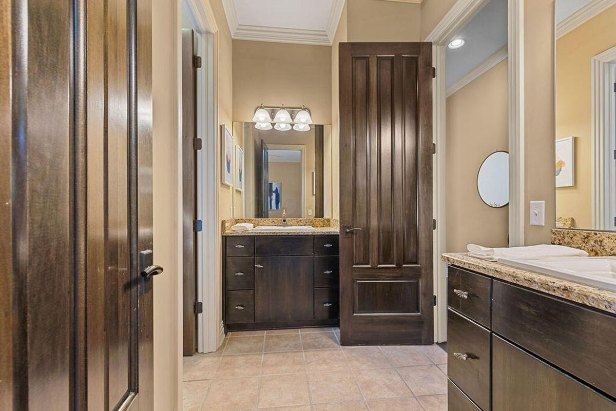 Bathroom features dual sinks with granite countertops, warm wood cabinetry, and a large mirror under recessed lighting.