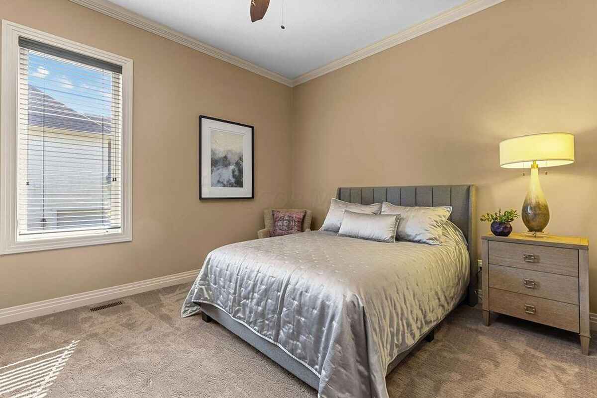 Bedroom includes a neatly styled bed with a soft headboard, a modern nightstand, and a window bringing in natural light.