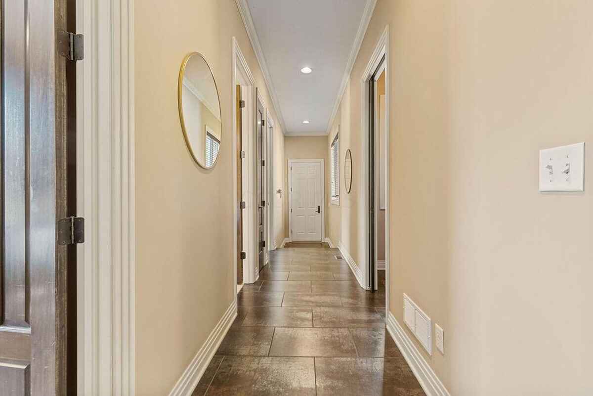 Hallway displays sleek tile flooring, neutral wall tones, and modern decor with framed mirrors and doors leading to adjacent rooms.