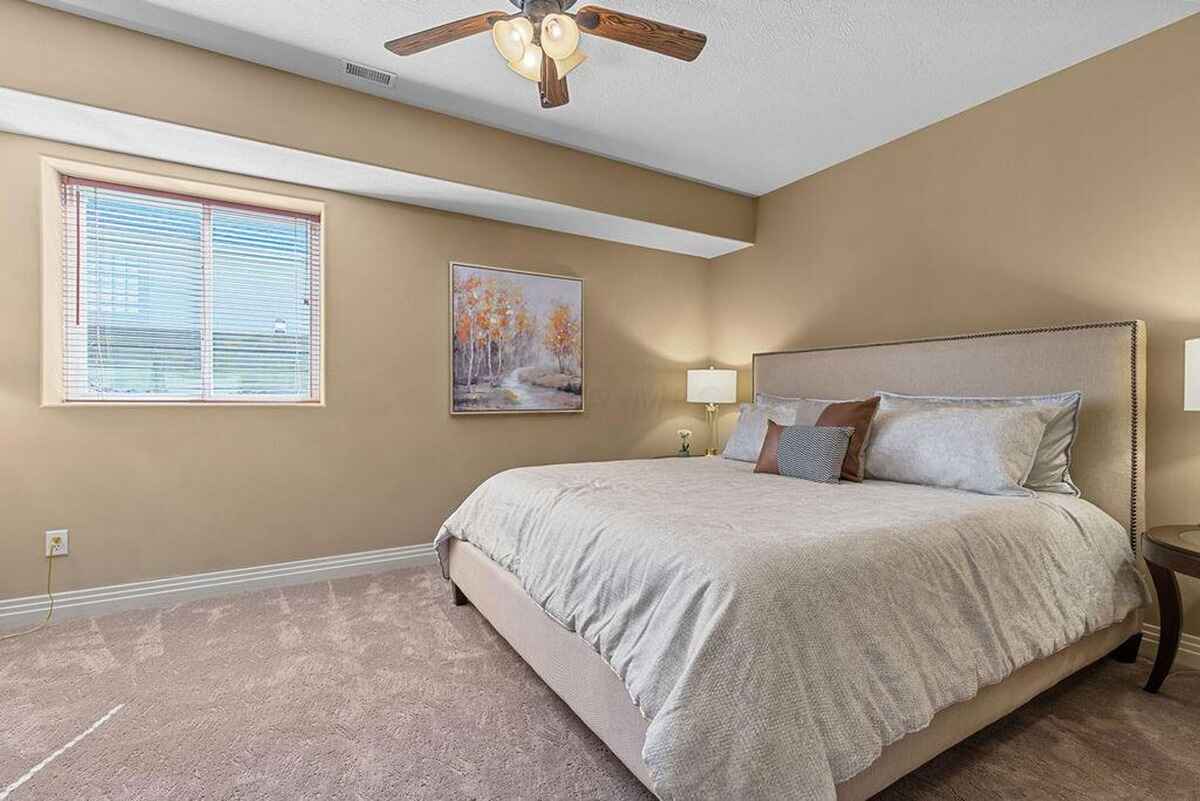 Spacious bedroom featuring a beige-toned color palette, a large window, and a ceiling fan with wooden blades.