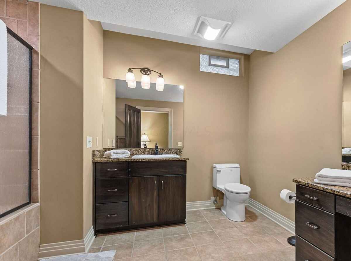 Modern bathroom with tiled flooring, dark wood cabinetry, granite countertops, and a glass-enclosed shower.