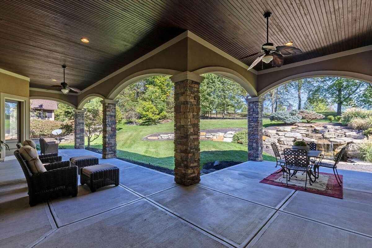 Covered patio with stone columns, ceiling fans, and a view of a landscaped backyard with a cascading water feature.