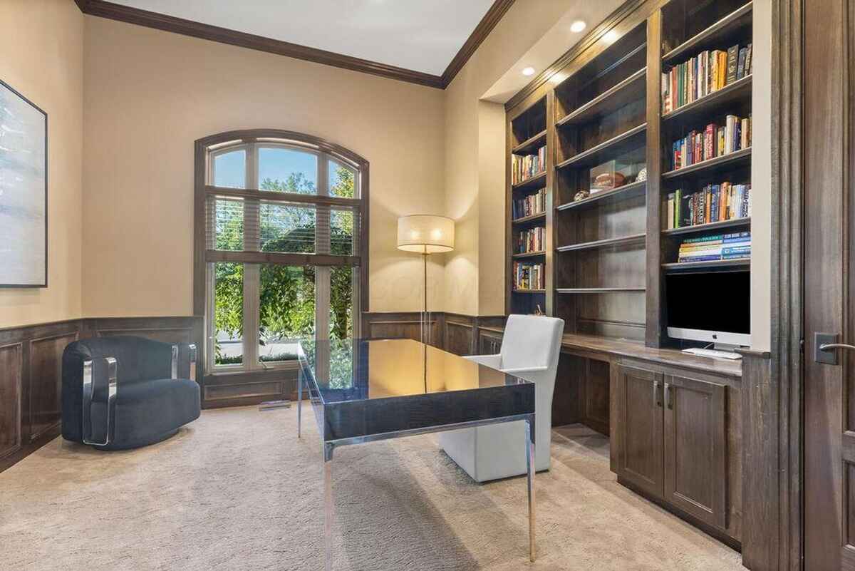 Study includes a built-in wooden bookshelf, arched window, and an organized workspace with a desk and chair.