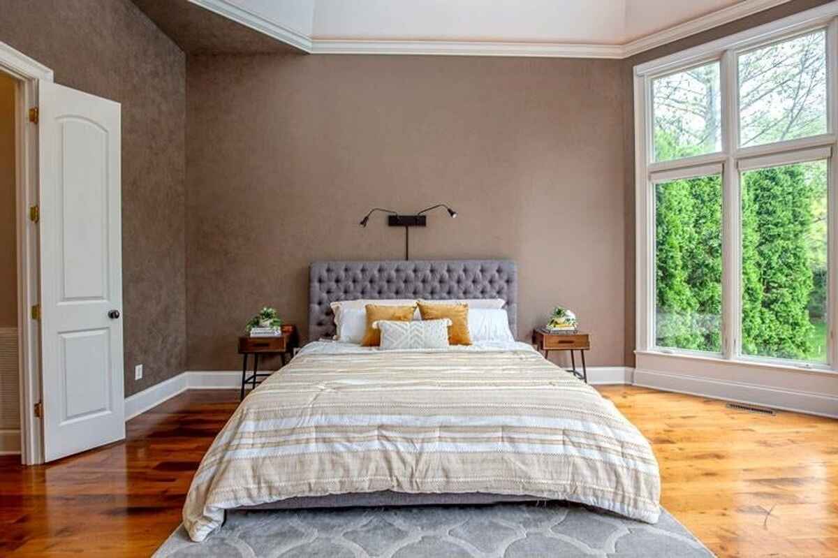 Bedroom featuring a tufted headboard, large windows, and hardwood flooring.