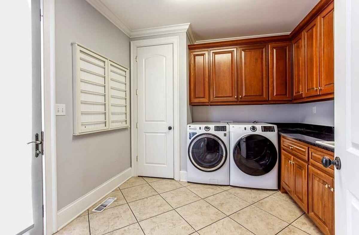 Laundry room with tiled flooring, front-load washer and dryer, and wooden cabinets for storage.