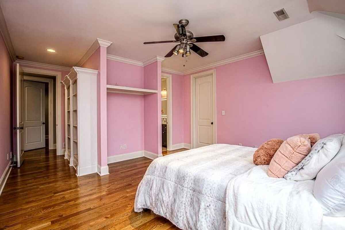 Bedroom with pink walls, built-in shelving, ceiling fan, and hardwood flooring.