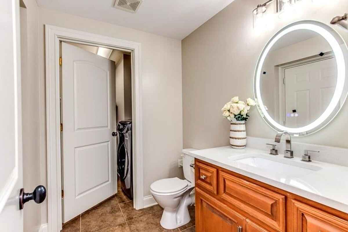 Bathroom with wooden cabinetry, circular LED mirror, and tiled flooring.