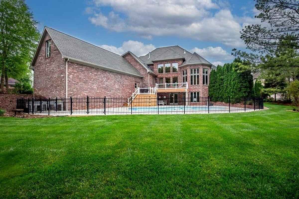 Brick home with a spacious backyard features a pool enclosed by a black wrought iron fence and a balcony overlooking the area.