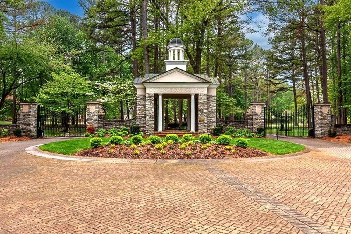 Gated entry surrounded by landscaped greenery and a stone structure with white columns marks the entrance to the neighborhood.