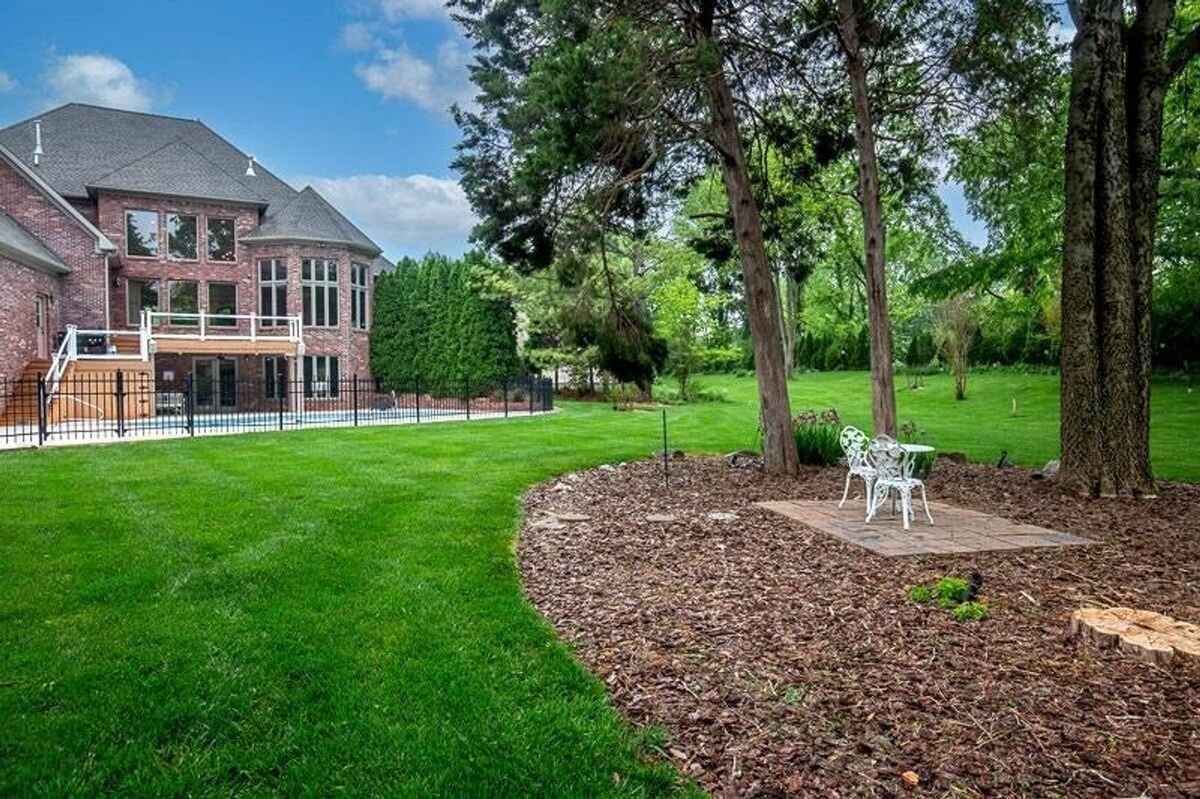 Backyard includes a sitting area surrounded by mulch under shaded trees, offering a view of the expansive lawn and pool.