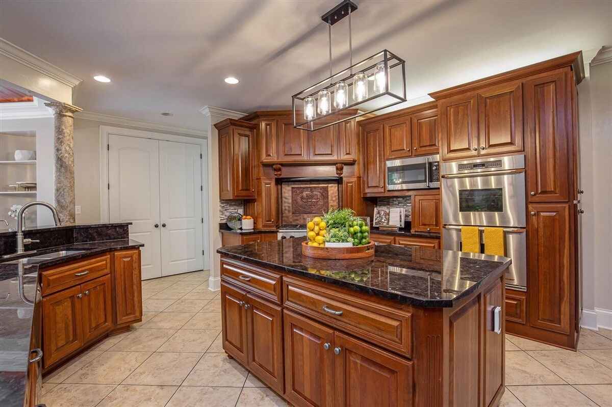 Kitchen featuring wooden cabinets, a center island with black countertop, and a contemporary light fixture.