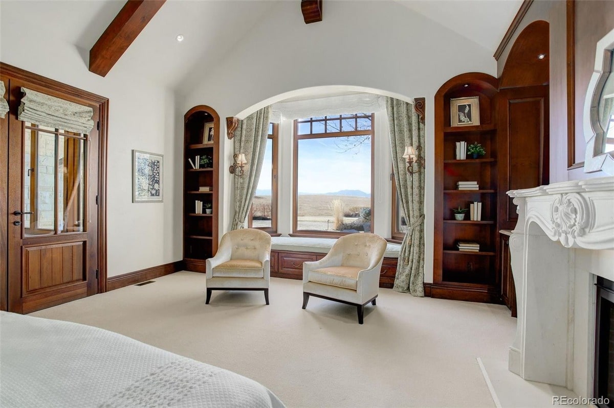 Elegant architectural details such as exposed beams and arched windows add to the grandeur of this master suite. The combination of a comfortable seating area and built-in bookshelves creates a space that is both luxurious and functional.