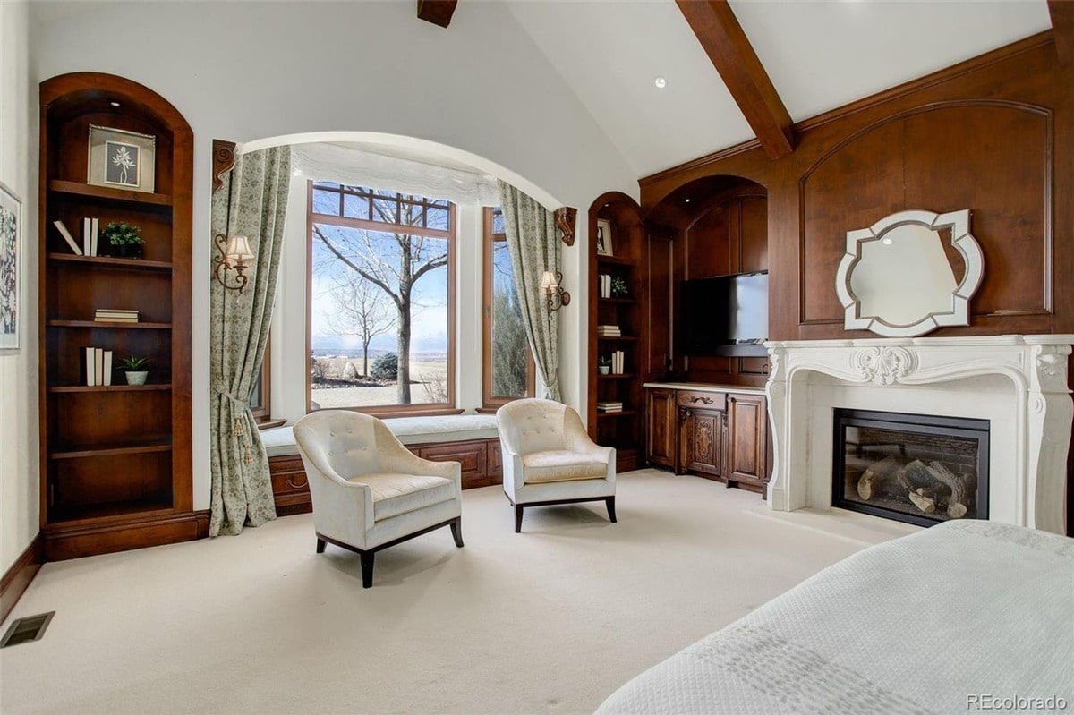 This luxurious master suite offers a serene retreat, featuring a stunning bay window with picturesque views and built-in bookshelves. The room's elegant design and comfortable seating create a sophisticated and inviting atmosphere.